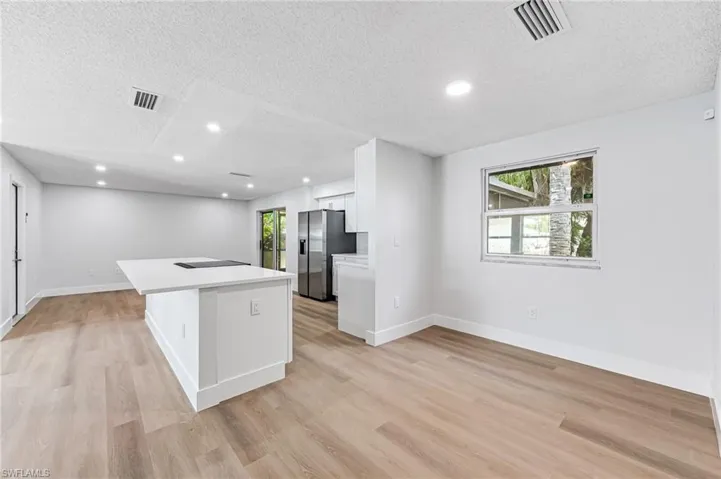 Kitchen featuring a textured ceiling, light hardwood / wood-style floors, white cabinets, and stainless steel fridge with ice dispenser