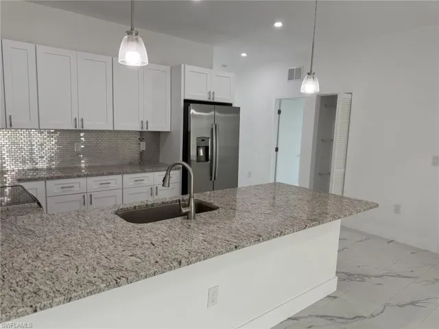 Kitchen featuring stainless steel fridge with ice dispenser, a sink, white cabinetry, light stone countertops, and recessed lighting