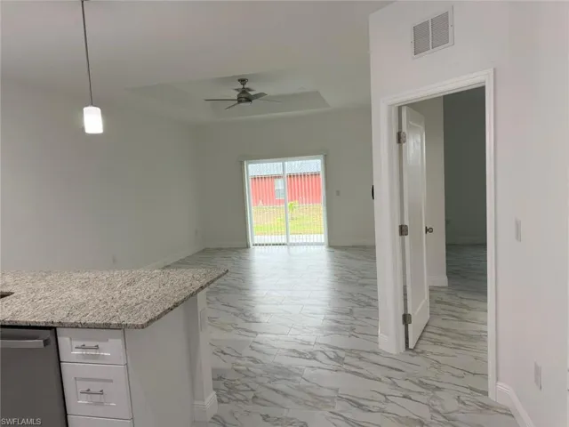 Kitchen with light marble finish flooring, a tray ceiling, a ceiling fan, baseboards, and white cabinets