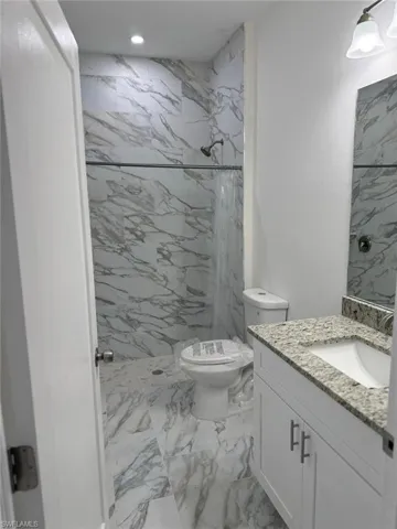Full bath with marble finish floors, toilet, a marble finish shower, vanity, and recessed lighting
