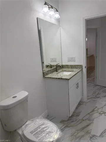 Half bathroom featuring marble finish flooring, toilet, and vanity