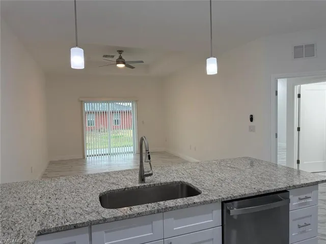 Kitchen featuring stainless steel dishwasher, a sink, a ceiling fan, open floor plan, and light stone countertops