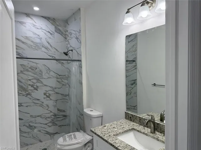 Full bathroom with toilet, vanity, and a marble finish shower