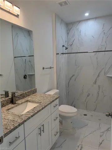 Bathroom featuring marble finish floors, vanity, toilet, a marble finish shower, and recessed lighting