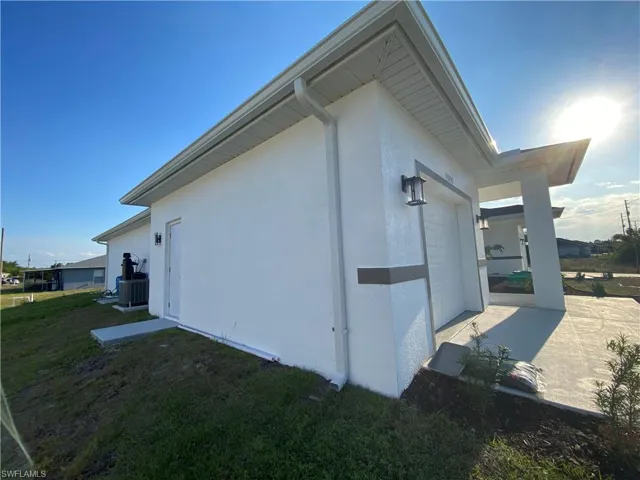 View of side of home with concrete driveway, central air condition unit, stucco siding, a yard, and a garage