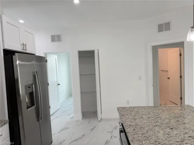 Kitchen with stainless steel refrigerator with ice dispenser, light marble finish flooring, white cabinetry, recessed lighting, and light stone counters