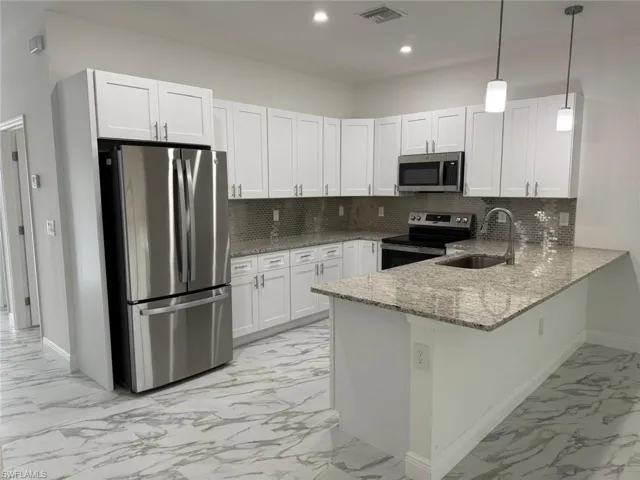 Kitchen with stainless steel appliances, a sink, light marble finish floors, baseboards, and a peninsula
