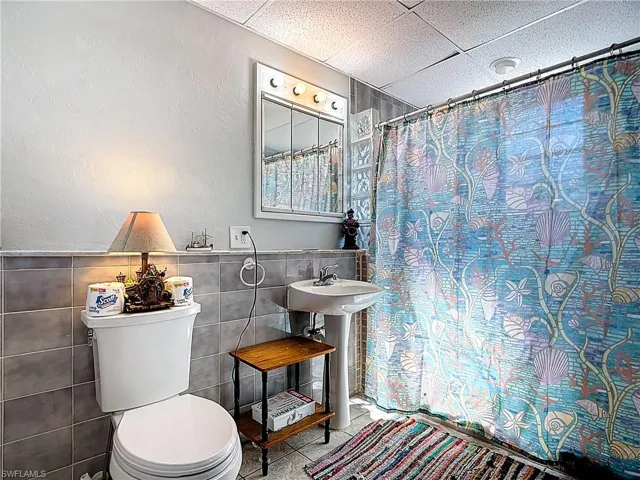Full bathroom with curtained shower, tile walls, a paneled ceiling, a textured wall, and wainscoting