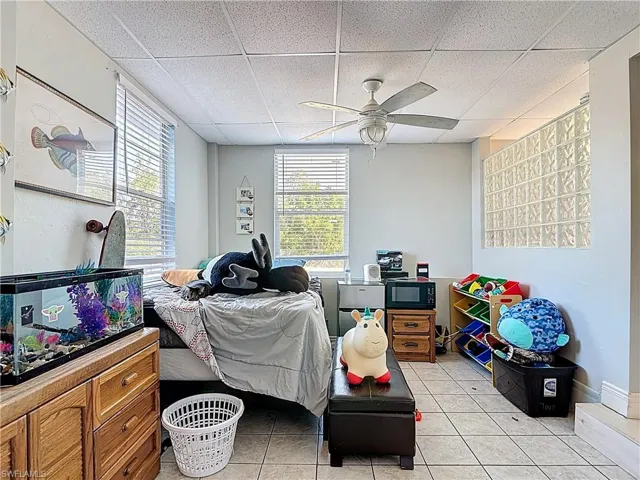 Bedroom featuring a drop ceiling, light tile patterned floors, and ceiling fan