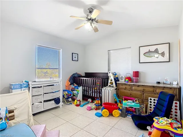 Bedroom with light tile patterned floors, ceiling fan, a nursery area, and lofted ceiling