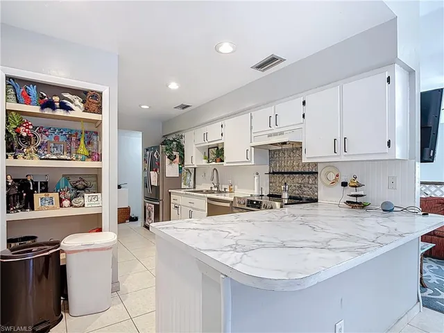 Kitchen featuring light countertops, a peninsula, white cabinets, decorative backsplash, and recessed lighting