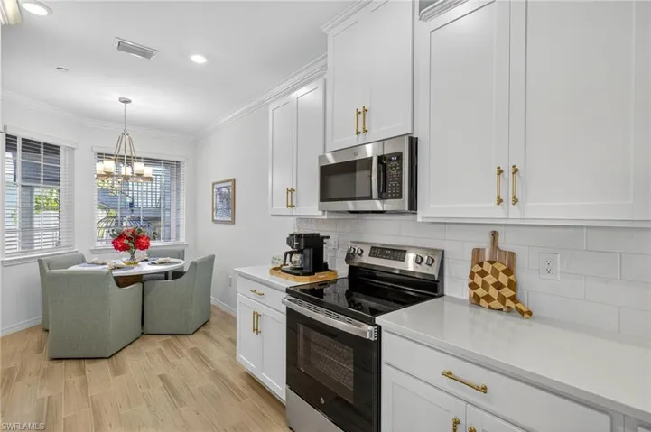 Kitchen with stainless steel appliances, ornamental molding, white cabinets, backsplash, and light wood-style flooring