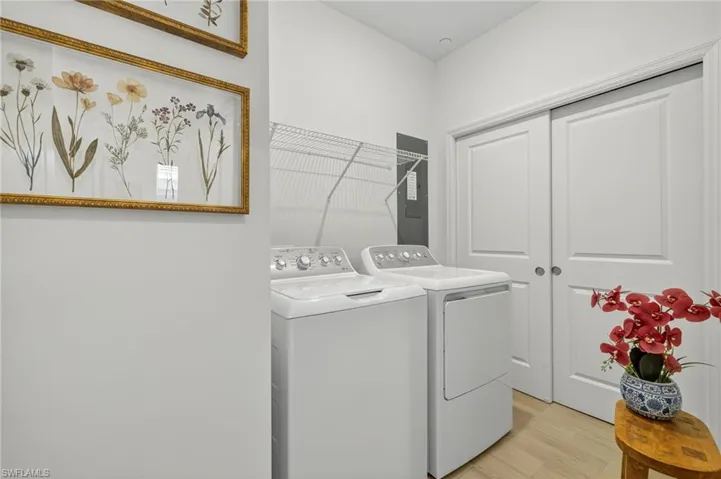 Laundry area with light wood-type flooring, washing machine and clothes dryer, and electric panel