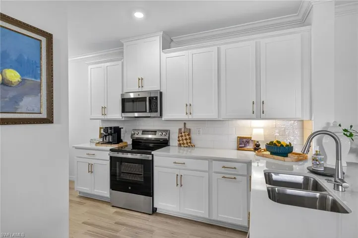 Kitchen with stainless steel appliances, decorative backsplash, white cabinets, ornamental molding, and light stone countertops