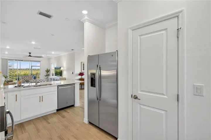Kitchen featuring stainless steel appliances, open floor plan, white cabinets, ornamental molding, and light wood-type flooring