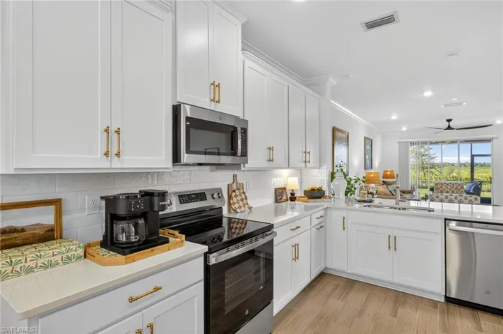 Kitchen with appliances with stainless steel finishes, light stone countertops, white cabinets, light wood-type flooring, and ceiling fan