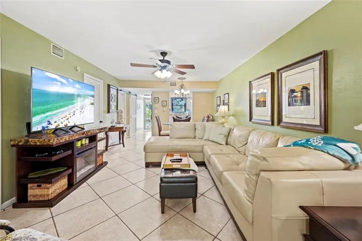 Tiled living room with ceiling fan with notable chandelier