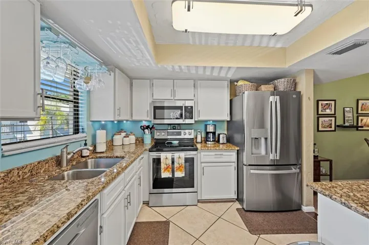Kitchen featuring sink, light tile patterned flooring, a tray ceiling, white cabinets, and appliances with stainless steel finishes