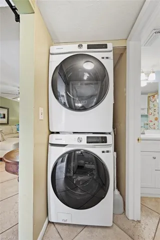 Laundry room featuring light tile patterned floors, ceiling fan, and stacked washer and clothes dryer
