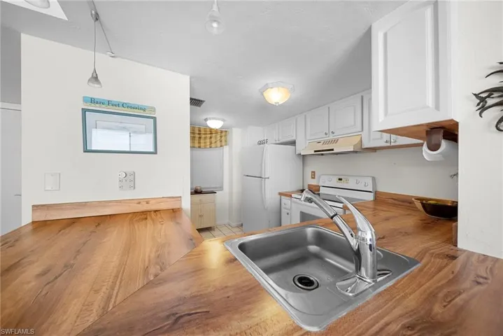 Kitchen featuring white cabinets, white appliances, decorative light fixtures, under cabinet range hood, and light tile patterned flooring