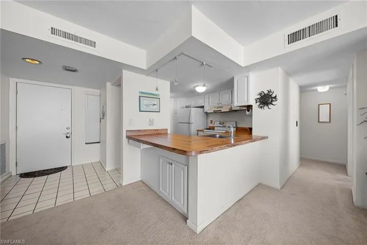 Kitchen with a peninsula, wood counters, light carpet, and white cabinetry