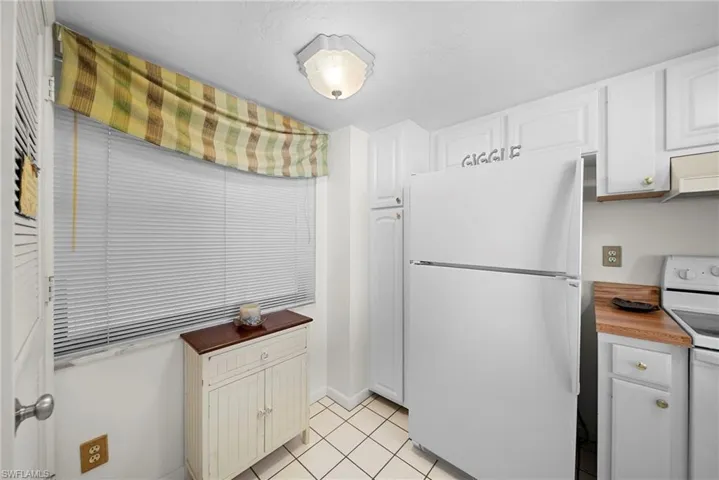 Kitchen featuring white appliances, white cabinetry, light tile patterned flooring, wall chimney exhaust hood, and wood counters