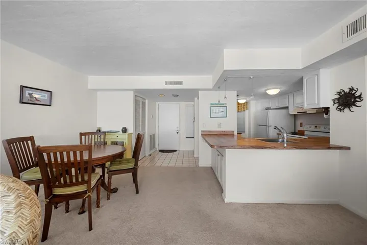 Kitchen with a peninsula, white appliances, butcher block counters, light carpet, and white cabinets