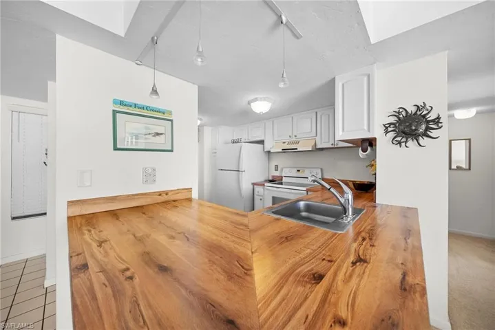 Kitchen with white appliances, hanging light fixtures, butcher block counters, white cabinetry, and under cabinet range hood