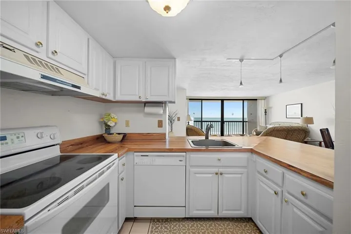 Kitchen featuring white appliances, white cabinetry, open floor plan, under cabinet range hood, and a peninsula
