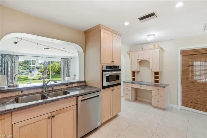 Kitchen featuring a double basin stainless steel sink, granite countertops, and light wood cabinetry