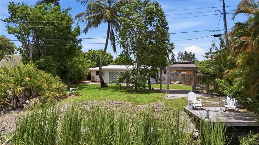 Waterfront property featuring a private wooden dock, a covered gazebo, mature palm trees, and a lush green lawn