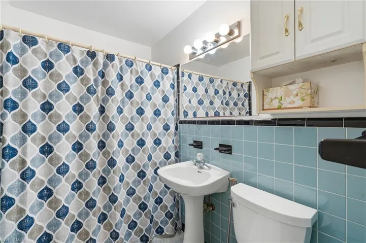 Bathroom featuring light blue wall tiles, a pedestal sink, and a white toilet