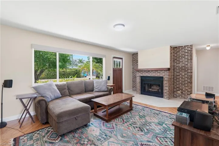 Living area featuring wood-finish flooring, a brick fireplace with a wood mantel, and a large window