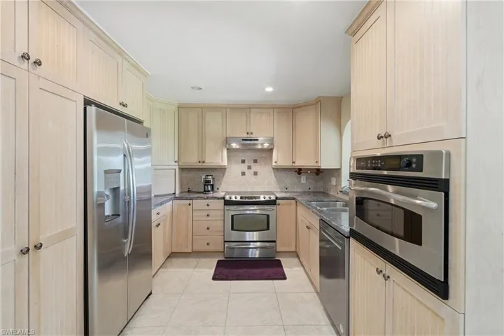 U-shaped kitchen featuring light wood cabinetry, stainless steel appliances, tile flooring, and a tiled backsplash