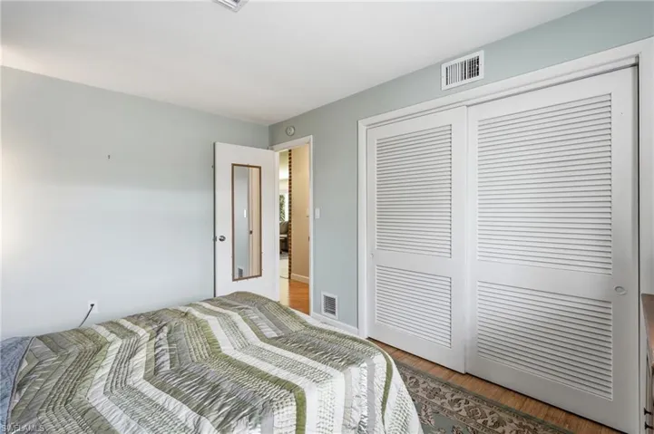 Bedroom featuring light blue wall paint, wood-finish flooring, and a pair of white louvered closet doors