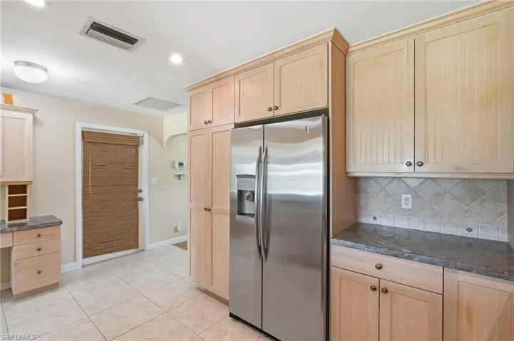 Kitchen featuring light wood-finish cabinetry, stainless steel refrigerator, stone countertops, and a tile backsplash