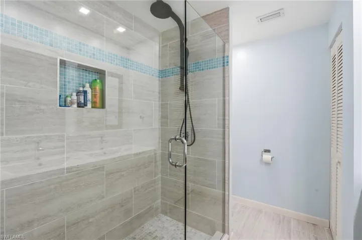 Spacious shower with large format grey tile, an integrated bench, and a mosaic tile accent band