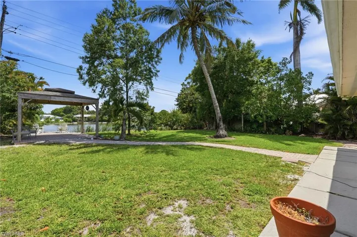 Grassed yard area featuring mature palm trees and a paved path leading to a waterside covered structure