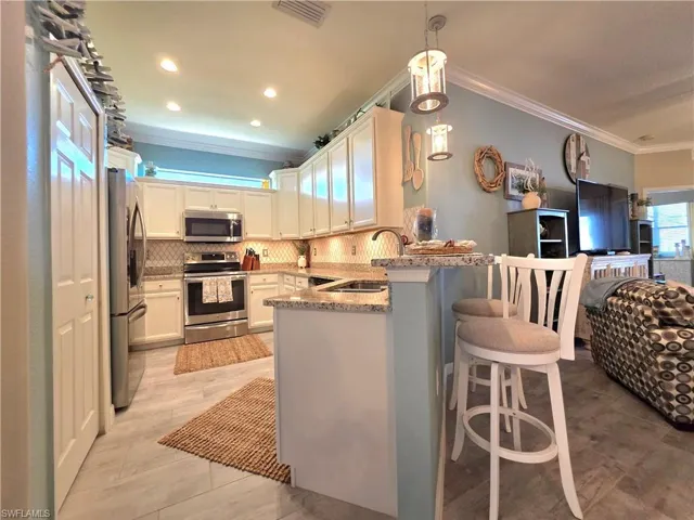 Kitchen with open floor plan, crown molding, a kitchen bar, stainless steel appliances, and light stone countertops