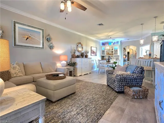 Living room with crown molding, arched walkways, and a ceiling fan