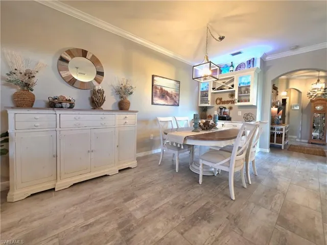 Dining room featuring arched walkways, ornamental molding, suspended lighting, and light wood-style flooring