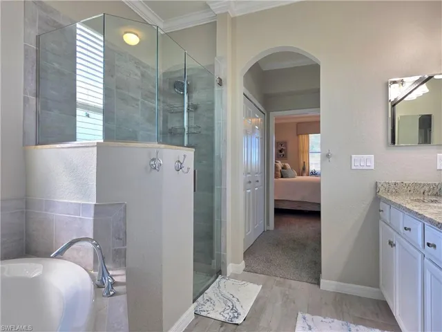 Ensuite bathroom with ornamental molding, vanity, tiled shower, a garden tub, and light wood-type flooring