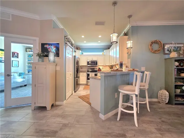 Kitchen featuring white cabinets, stainless steel appliances, a kitchen bar, tasteful backsplash, and ornamental molding