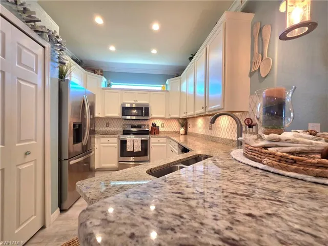 Kitchen featuring light stone counters, stainless steel appliances, white cabinetry, decorative backsplash, and recessed lighting