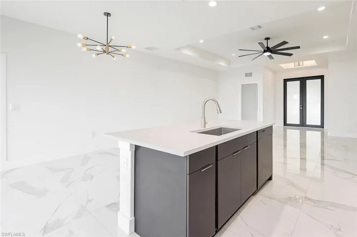 Kitchen with open floor plan, french doors, a raised ceiling, light marble finish floors, and an island with sink