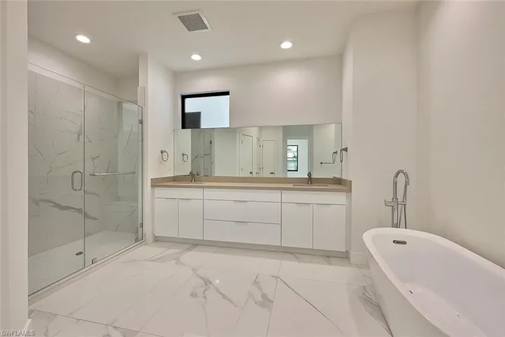 Full bathroom featuring a soaking tub, light marble finish flooring, double vanity, a marble finish shower, and recessed lighting