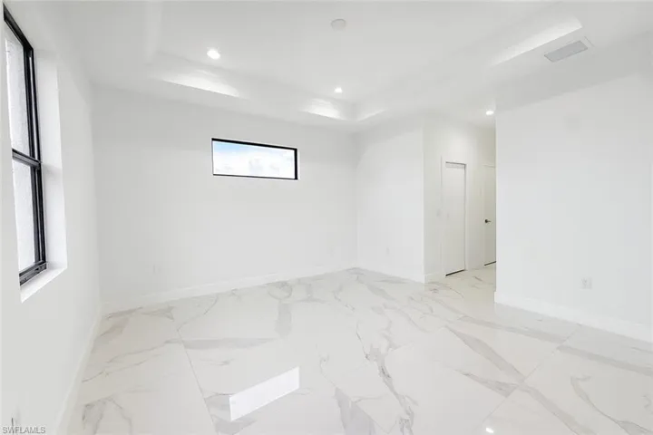 Empty room featuring a tray ceiling, recessed lighting, and light marble finish flooring