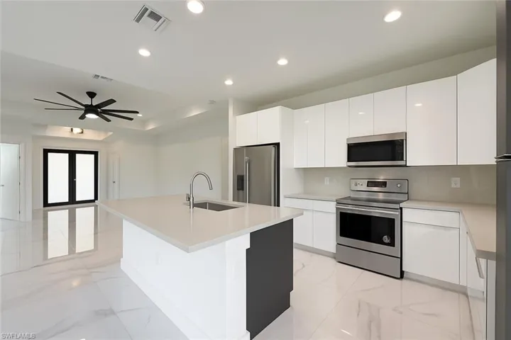 Kitchen with stainless steel appliances, light marble finish flooring, modern cabinets, white cabinets, and an island with sink