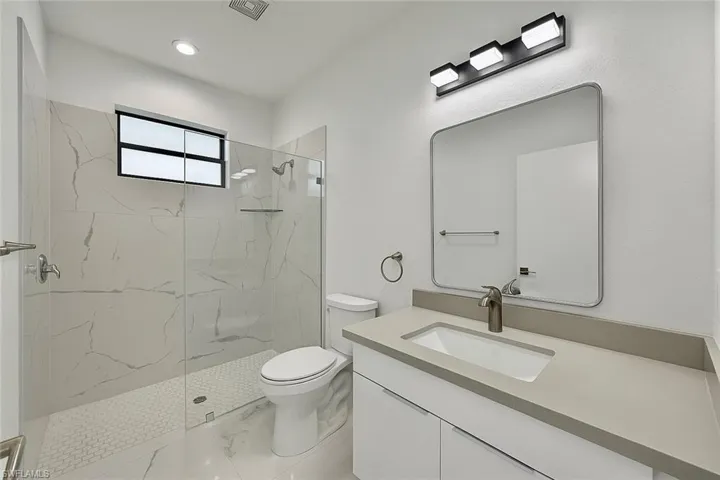 Bathroom featuring a marble finish shower, vanity, marble finish floors, and recessed lighting