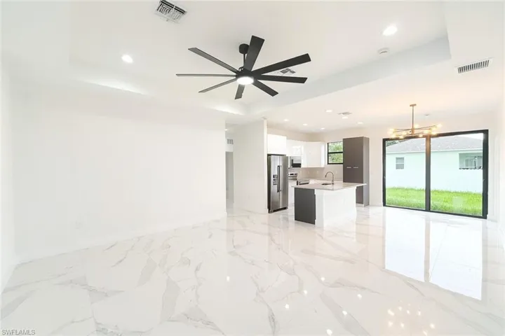 Kitchen with open floor plan, a tray ceiling, a chandelier, light marble finish flooring, and recessed lighting
